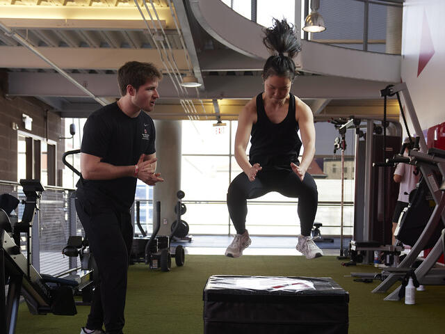 Personal trainer coaches a participant during a box jump in the RPAC Fitness Suite.